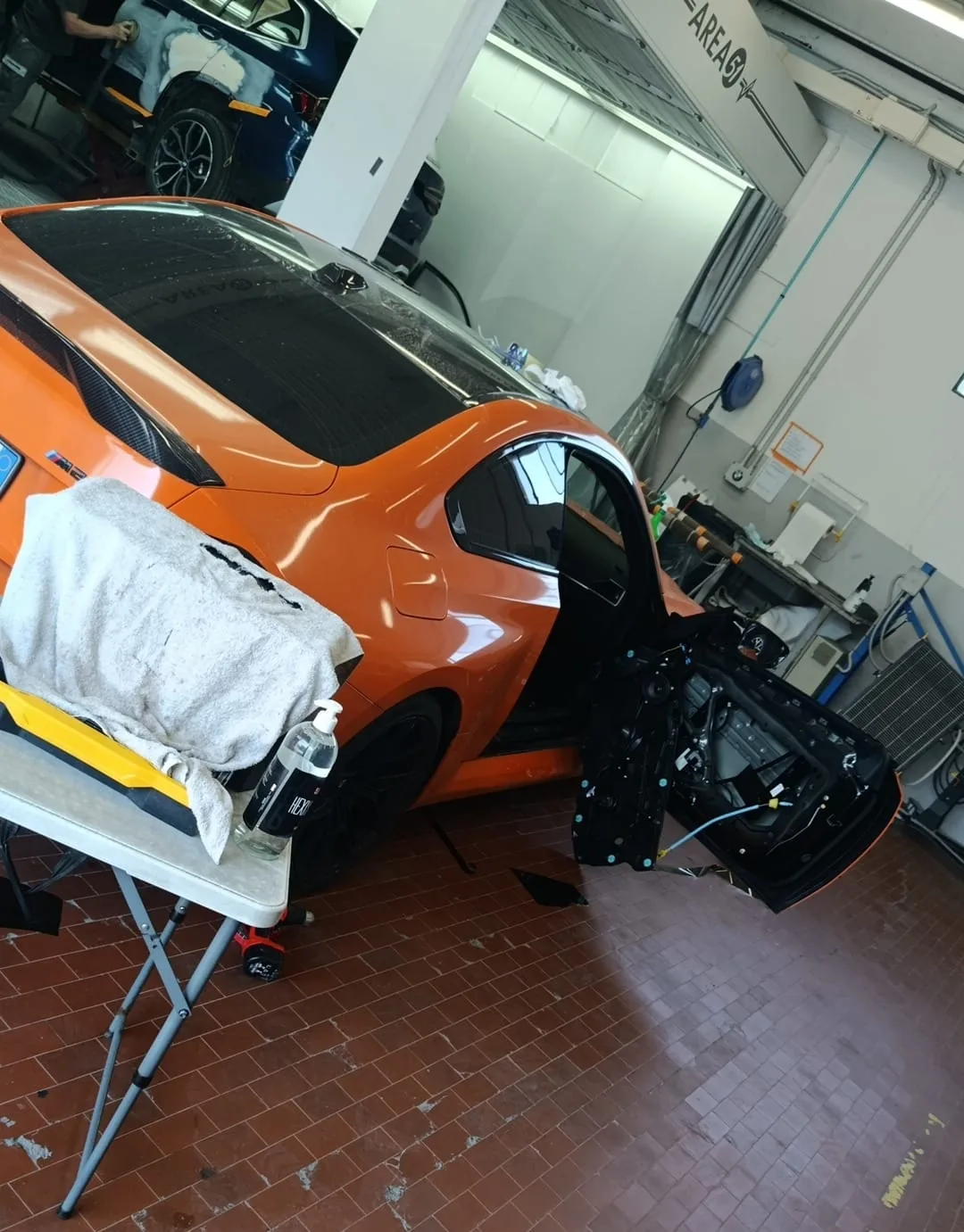 BMW M2 arancione con la portiera smontata durante l'oscuramento dei vetri nel laboratorio Metrix